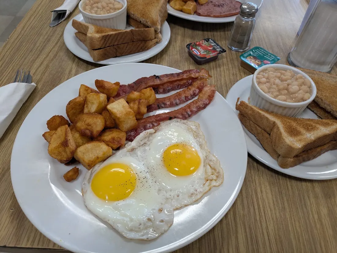 Breakfast plate with sunny-side-up eggs, bacon, toast, potatoes and a cup of beans
